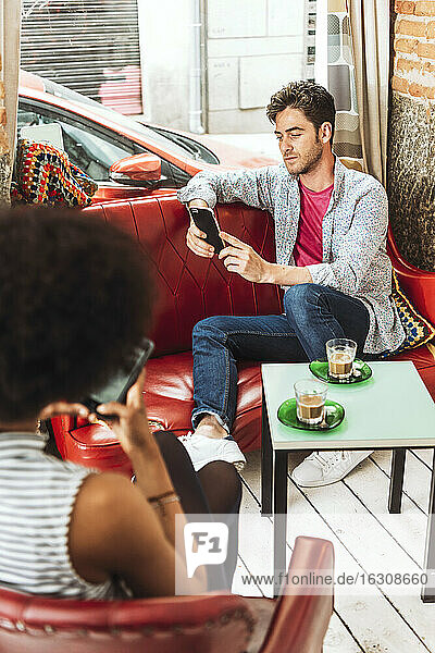 Pärchen mit Kaffee auf dem Tisch  das im Restaurant sitzt und Mobiltelefone benutzt