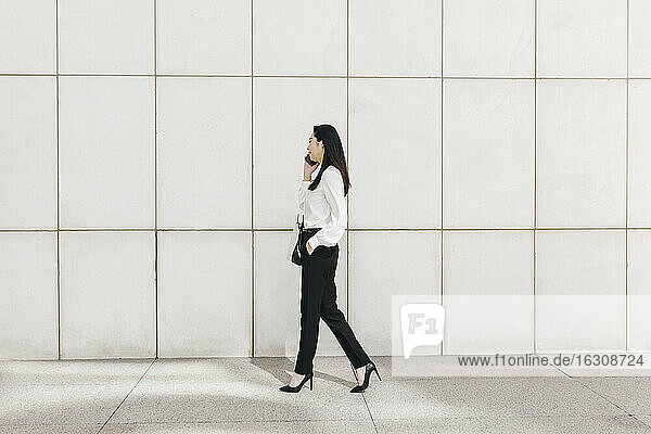 Businesswoman walking while talking on smart phone in city