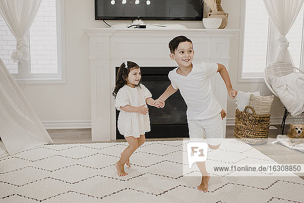 Playful siblings holding hands while running in living room
