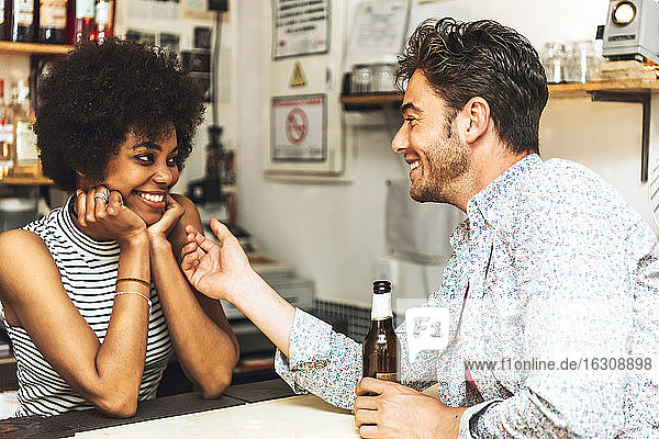 Mann hält Bierflasche und berührt Barkeeperin  während er mit ihr an der Theke flirtet