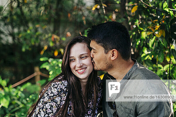 Junger Mann mit geschlossenen Augen küsst lächelnde Frau im Park