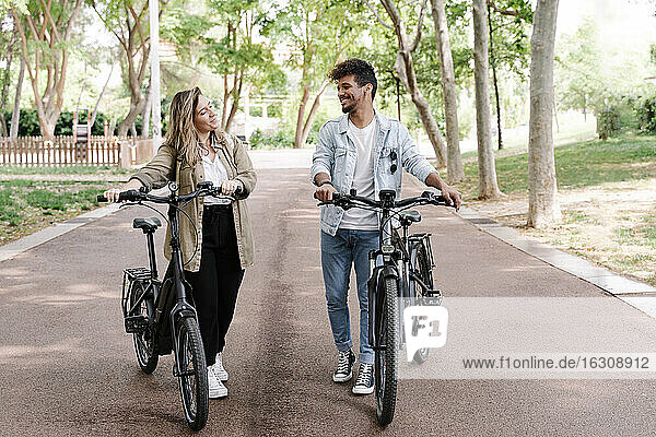 Lächelndes junges Paar mit Elektrofahrrädern auf der Straße