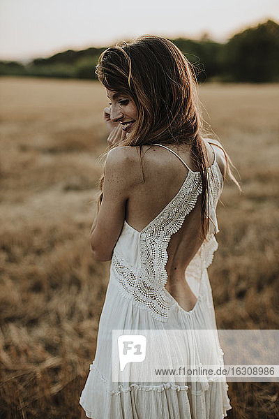 Frau im weißen Kleid schaut über die Schulter  während sie in einem Weizenfeld steht