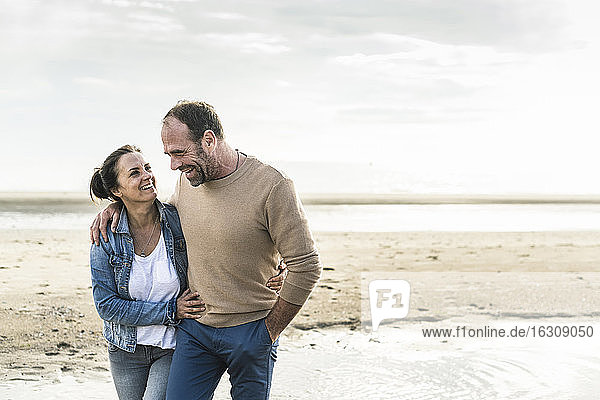 Cheerful mature couple embracing while standing against sea during weekend
