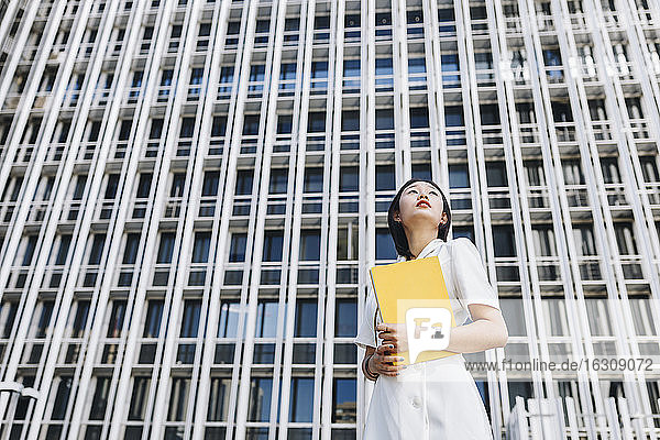 Businesswoman holding book while standing against downtown district in city