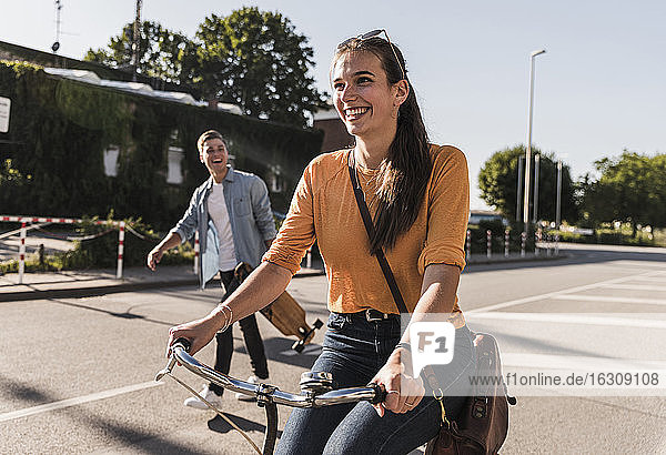 Happy young woman riding bicycle while boyfriend walking on street in city