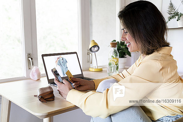 Happy young woman using credit card and smart phone for online shopping at home