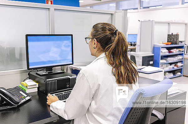 Pharmazeutin  die im Krankenhaus sitzend einen Computer auf dem Schreibtisch benutzt