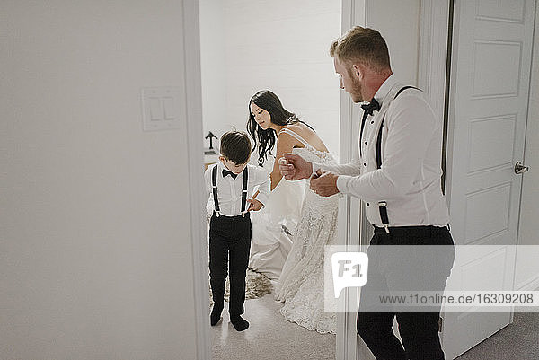 Mutter zieht ihren Sohn für die Hochzeit an,  während der Vater zu Hause in der Tür steht