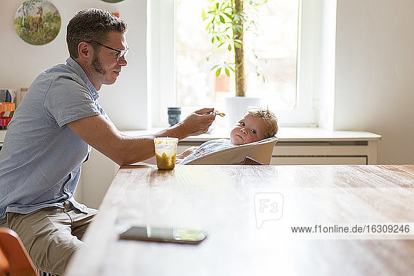 Father feeding baby boy while sitting by dining table at home