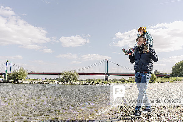 Vater  der seine Tochter auf der Schulter trägt  während er am Flussufer steht