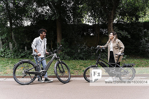 Smiling couple standing with electric bicycles on road