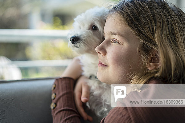 Cute girl embracing dog while looking away in living room