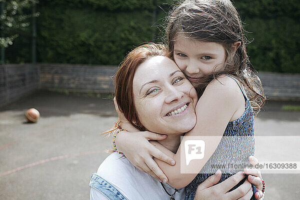 Mädchen umarmt lächelnde Mutter am Basketballplatz im Hinterhof