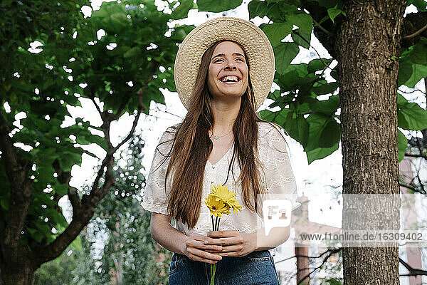Lächelnde Frau schaut weg  während sie gelbe Blumen in einem öffentlichen Park im Frühling hält