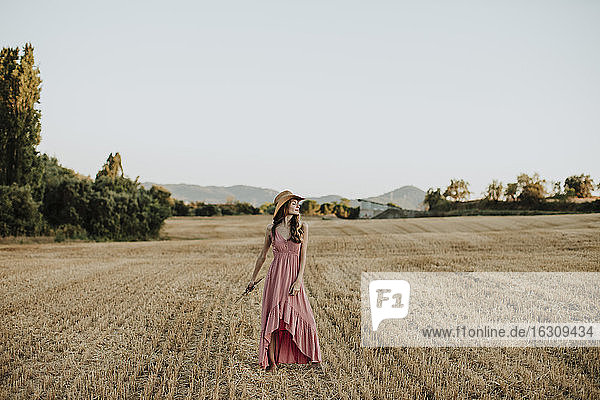 Woman wearing dress while standing at wheat field against clear sky during sunset