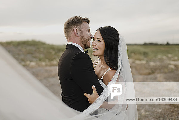 Lächelnder Bräutigam  der seine Braut umarmt  während er im Feld vor dem Himmel steht