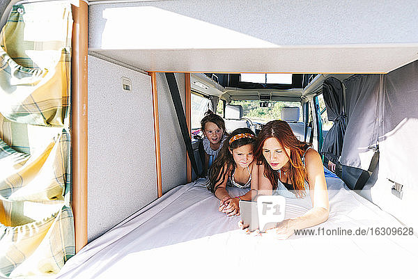Mother with daughters using digital tablet while lying on bed in motor home