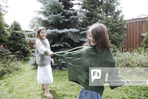 Verspieltes Mädchen zieht am Pulloverärmel der Schwester im Hinterhof