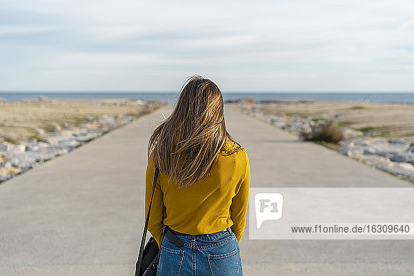 Frau mit Tasche auf dem Fußweg zum Meer stehend