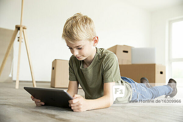 Boy with blond hair using digital tablet while lying on floor in new house