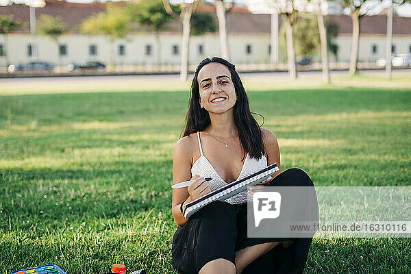 Lächelnde Frau  die im Gras sitzend in einem öffentlichen Park malt