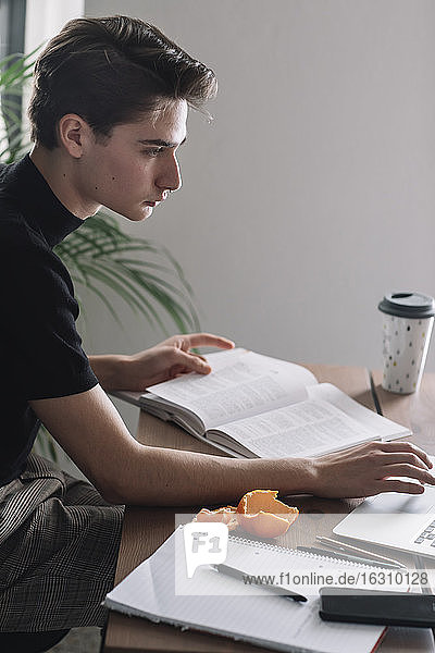Gutaussehender männlicher Student  der einen Laptop benutzt  um am Tisch Hausaufgaben zu machen