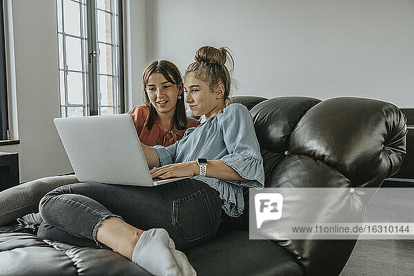 Freunde benutzen einen Laptop  während sie sich auf dem Sofa zu Hause entspannen