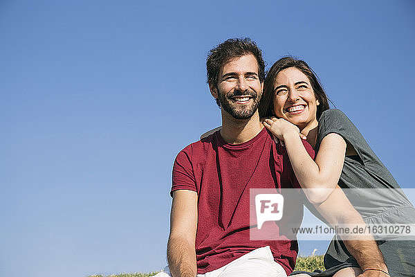Smiling woman leaning on man shoulder while sitting against clear sky