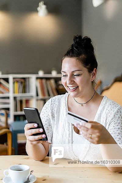 Lächelnde üppige Frau beim Online-Shopping über Handy in einem Café