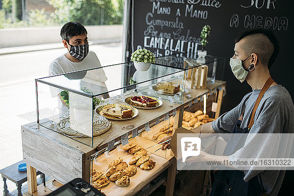 Kellner und Kunde mit Schutzmasken am Tresen eines Cafés