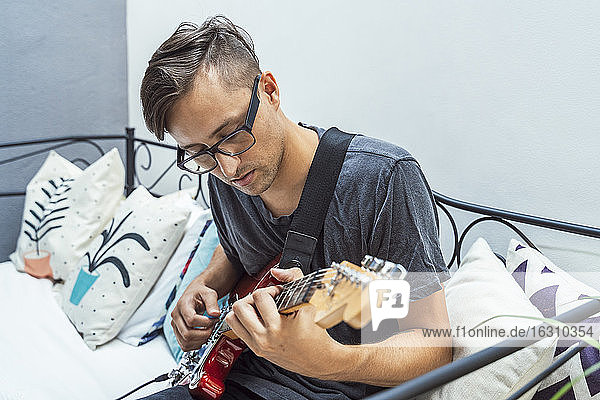 Musician practicing guitar on sofa at home