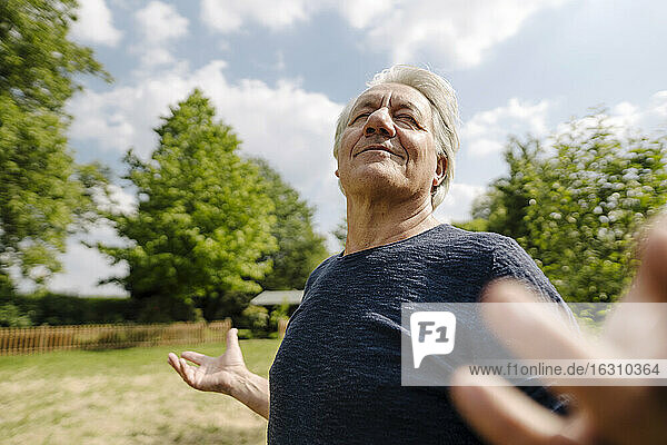 Confident wrinkled man with eyes closed enjoying in field during sunny day