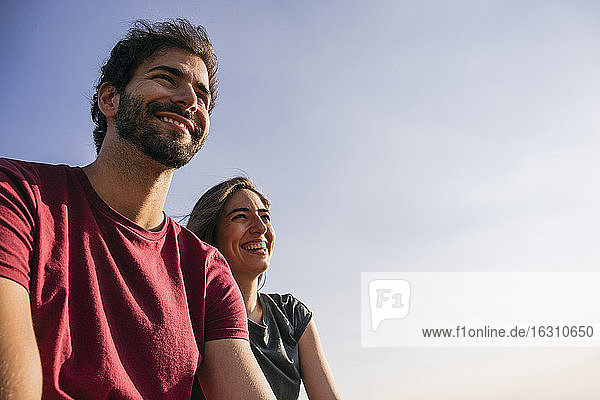 Smiling couple looking away while sitting against clear sky