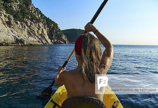 Woman kayaking while sitting in boat against clear sky
