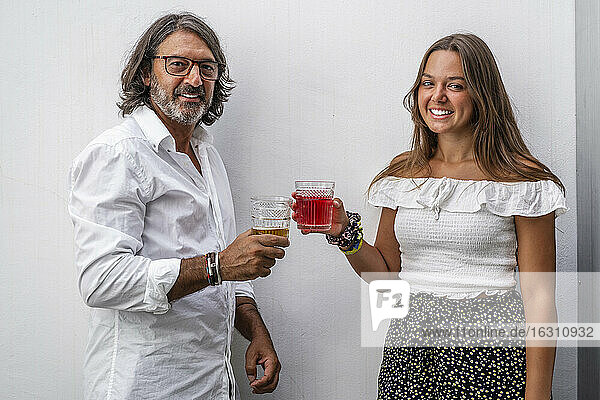 Smiling father toasting drinks with daughter while standing against wall