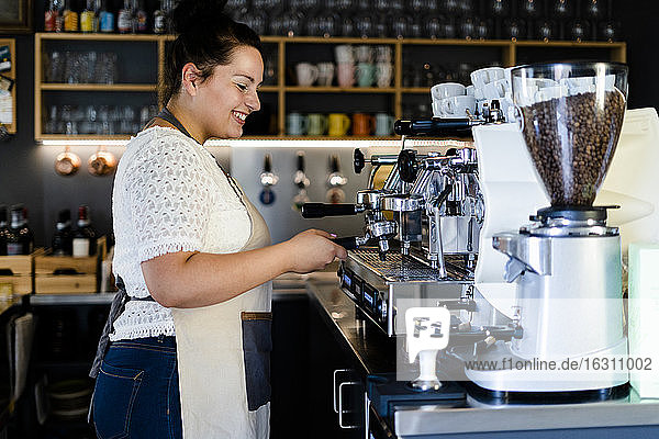 Lächelnde Barista-Frau  die Kaffee durch eine Maschine in einem Café zubereitet