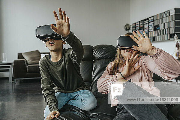Fröhliche Freunde  die zu Hause auf der Couch sitzen und durch Virtual-Reality-Simulatoren schauen