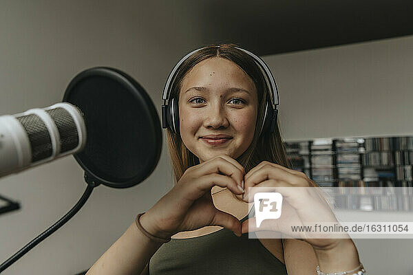 Close-up of smiling teenage girl making heart shape while singing in recording studio