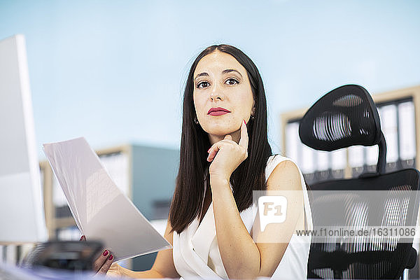 Geschäftsfrau sitzt am Schreibtisch und hält ein Dokument