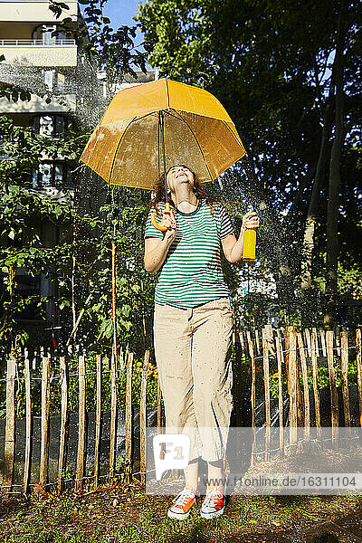 Junge lachende Frau mit Regenschirm und Limonade im Garten