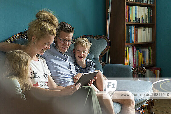 Familie teilt sich ein digitales Tablet  während sie zu Hause auf dem Sofa sitzt