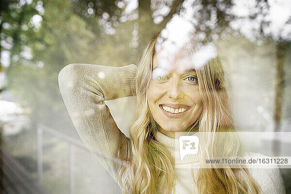 Nahaufnahme einer lächelnden Geschäftsfrau mit blondem Haar in einem Büro  gesehen durch ein Fenster