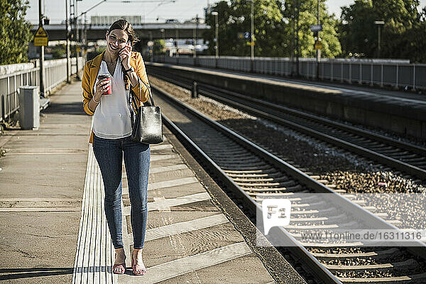 Lächelnde Frau  die auf dem Bahnsteig stehend mit ihrem Handy telefoniert