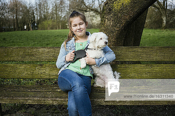 Lächelndes Mädchen mit Hund sitzt auf einer Bank im Park