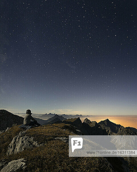 Deutschland  Bayern  Mann sitzt auf dem Gipfel der Ammergauer Hochplatte in der Abenddämmerung