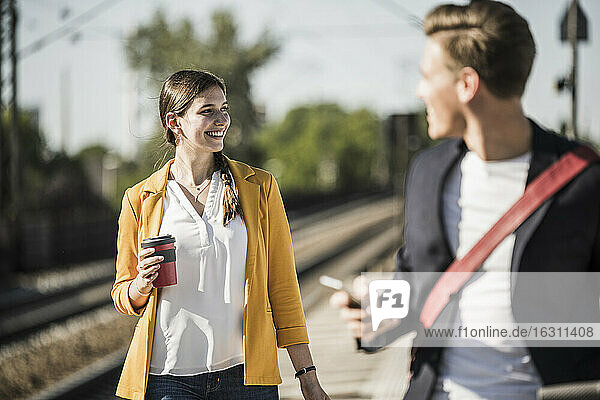 Lächelnde Frau mit wiederverwendbarem Kaffeebecher  die beim Gehen am Bahnsteig wegschaut