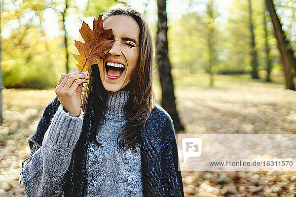 Junge lachende Frau hält Herbstlaub auf ihrem Auge