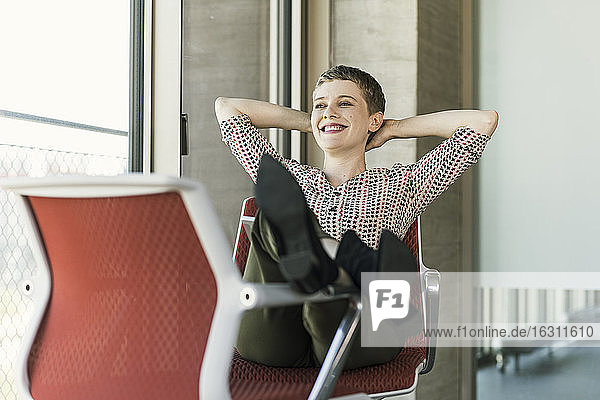 Lächelnde Geschäftsfrau  die auf einem Stuhl im Büro sitzt und eine Pause macht
