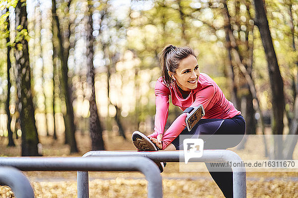 Junge Joggerin streckt ihr Bein auf einem Fahrradständer im Herbstwald